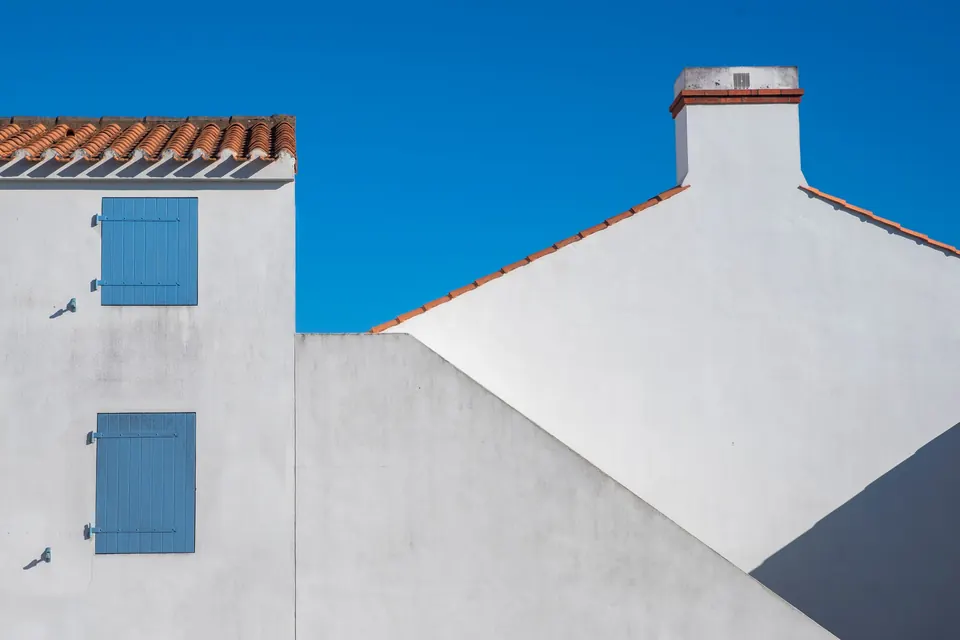 Pignons blancs, volets bleus et bordure de tuiles sous un ciel dégagé